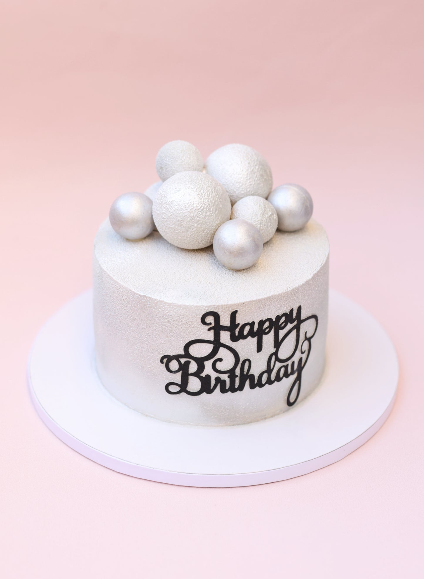 A beautifully decorated Strawberry Plombir Cake featuring a velvety finish, strawberry confit filling, and elegant Belgian chocolate spheres.