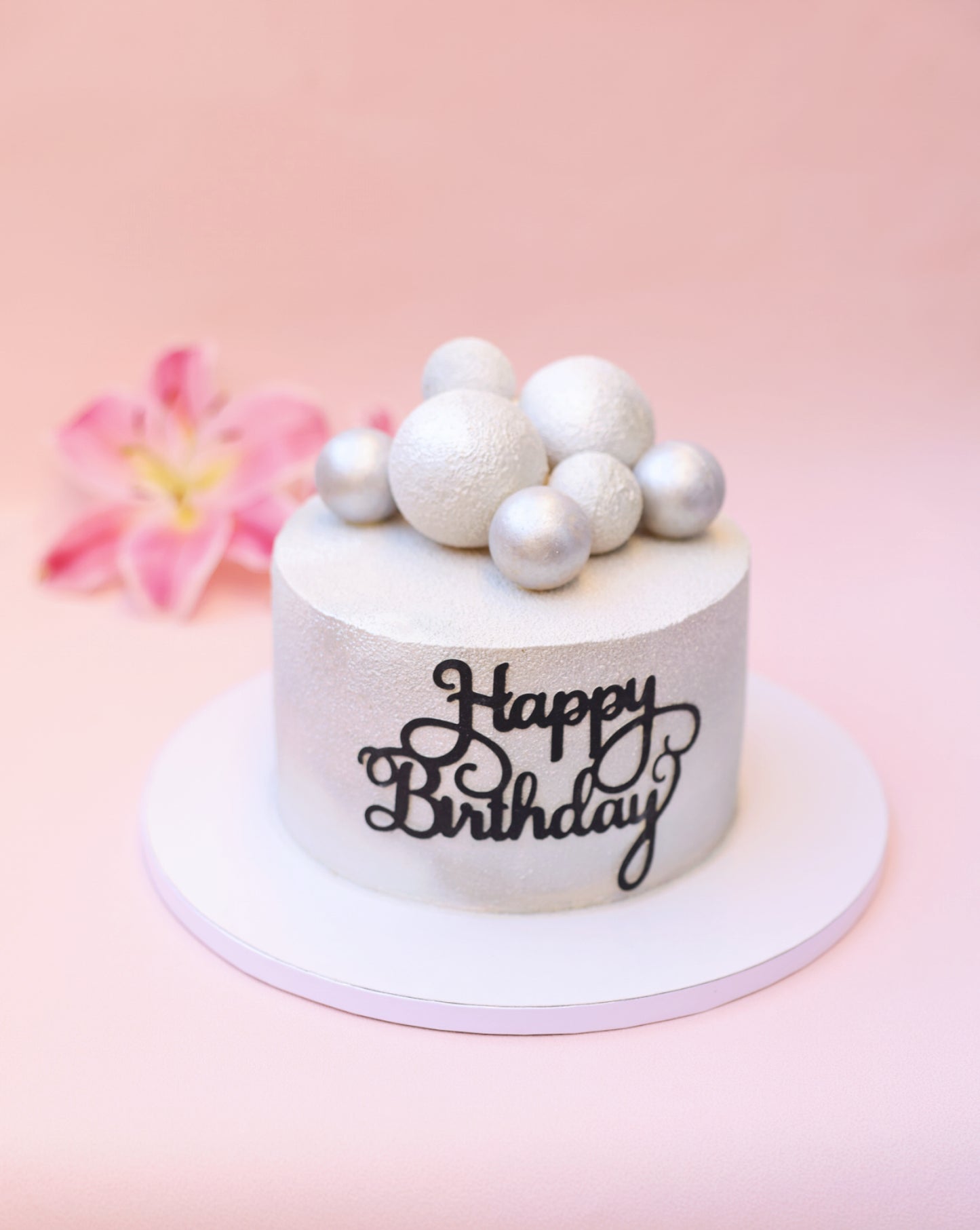 A beautifully decorated Strawberry Plombir Cake featuring a velvety finish, strawberry confit filling, and elegant Belgian chocolate spheres.