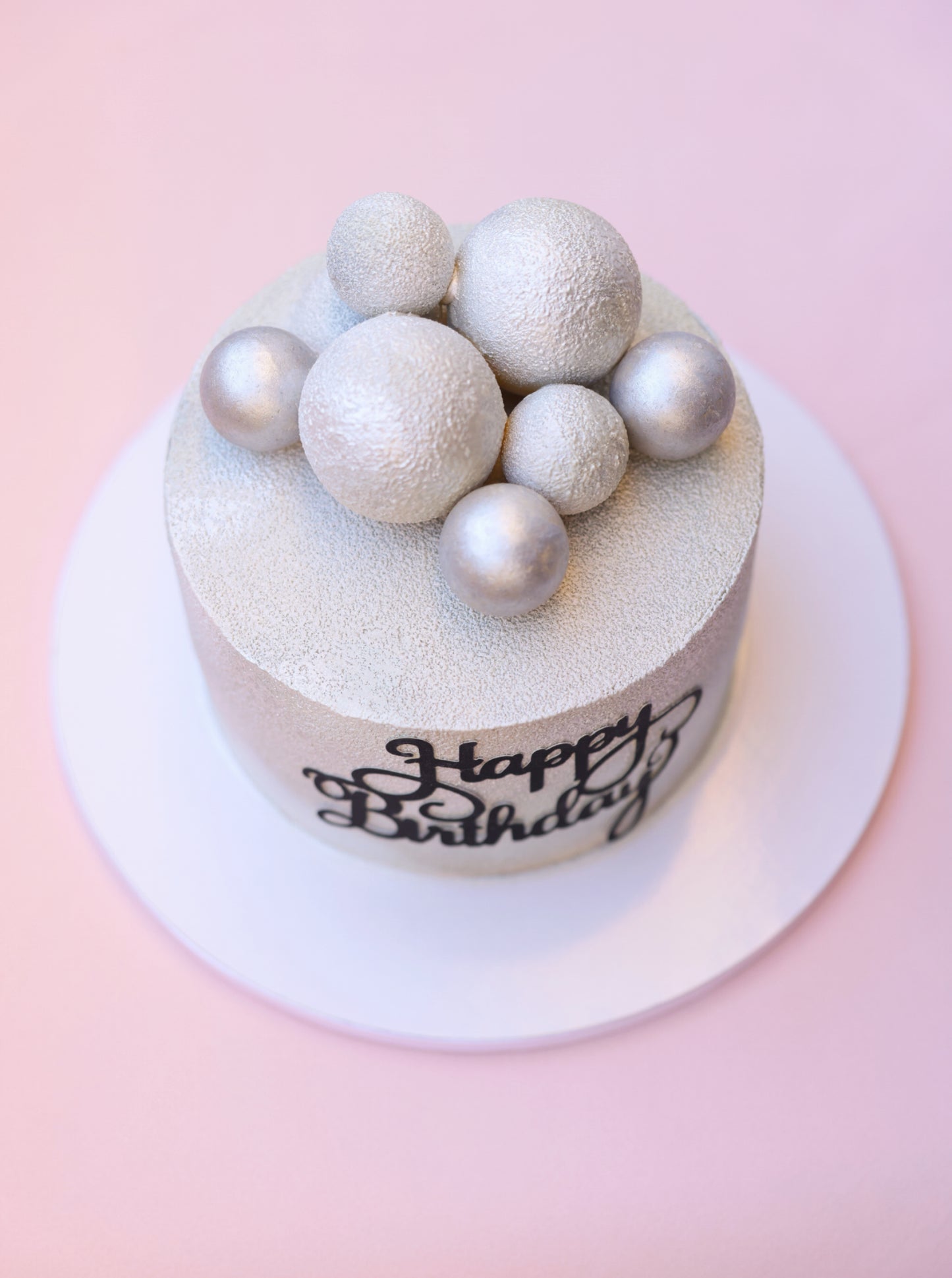 A beautifully decorated Strawberry Plombir Cake featuring a velvety finish, strawberry confit filling, and elegant Belgian chocolate spheres.