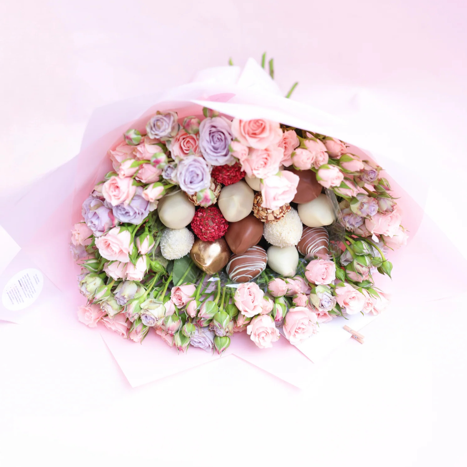 Premium bouquet of fresh pink and lavender roses with chocolate-covered strawberries, arranged as an elegant gift.